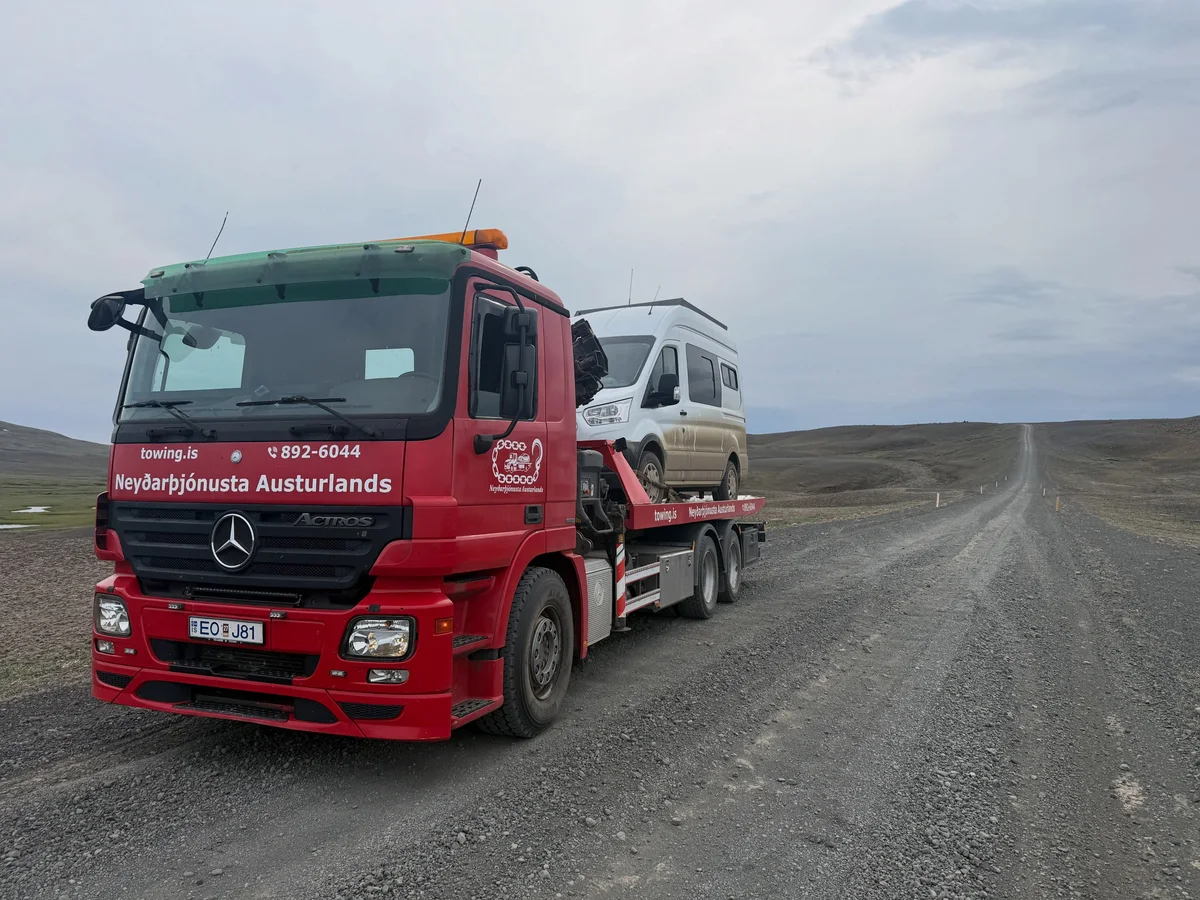 Rauður bílaflutningabíll Towing.is með húsbíl á pallinum á malarvegi